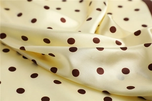 Close-up of yellow satin fabric with brown polka dots showing smooth silk texture