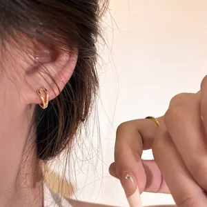 Detail of elegant 18K gold layered hoop earrings and green gemstone ring on a model