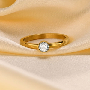 Detailed view of a gold plated ring with a round zircon on champagne silk fabric