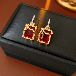 Détail de boucles d'oreilles carrées dorées avec pierre rouge et zircons étincelants