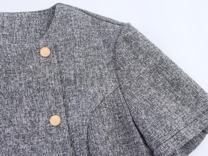 Close-up of grey tweed fabric texture and decorative gold textured buttons on the jacket