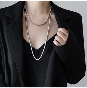 Detail of minimalist silver snake bone necklaces layered over a classic black blazer