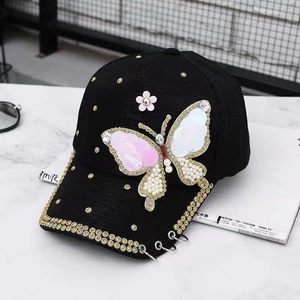 Gros plan d'une casquette noire avec papillon pailleté, strass dorés et anneaux métalliques