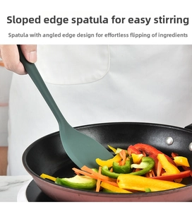 Close-up of silicone spatula with beveled edge stir-frying vegetables in a non-stick pan
