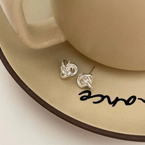 Dettaglio degli orecchini a nodo in argento su un piatto in ceramica minimalista