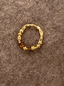 Detail view of 18K gold plated tiger eye ring with wavy texture on brown fabric
