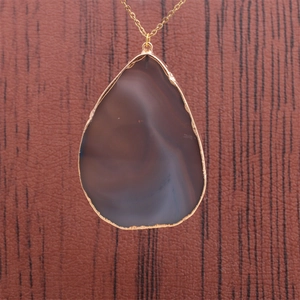 Gros plan sur un pendentif en agate goutte d'eau avec bordure dorée et chaîne fine