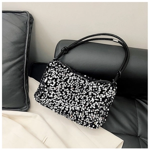 Close-up of silver sequined shoulder bag with black leather handle on a stylish sofa