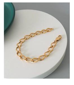 Detailed shot of gold-plated chunky link bracelet with lobster clasp on a white pedestal
