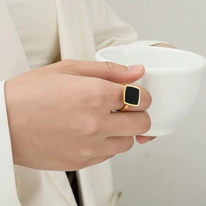 Minimalist gold ring with square black stone on model holding a white cup