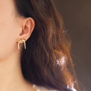 Close-up of golden bow-shaped stud earrings with tassel fringe on female ear