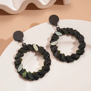 Macro detail of geometric acrylic earrings with green stone fragments on a white tray
