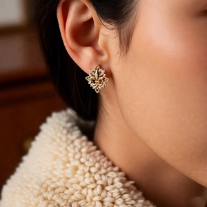 Close-up of 18k gold plated fleur-de-lis stud earring with zircon on a model's ear