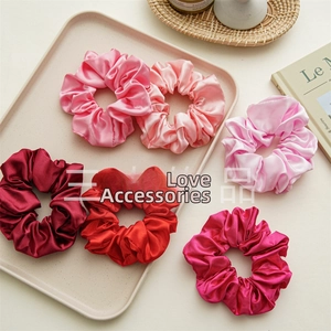 Close-up of six assorted red and pink satin scrunchies in various shades on a beige tray