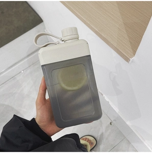 Gray square plastic water bottle with beige handle being held in a hand
