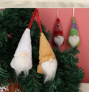 Detail von vier gestrickten Weihnachtswichteln mit weißen Bärten an einem Tannenzweig