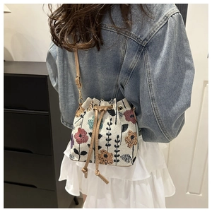 Detail of floral knit drawstring bucket bag with colorful embroidery and faux leather strap
