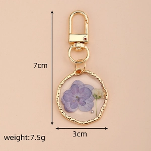 Detail of floral resin keychain with dried flowers and gold clasp on pink background