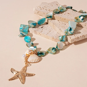 Irregular blue shell necklace with golden starfish and pearl on textured stone