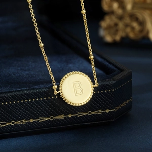 Macro shot of gold letter B pendant necklace with micro-bead border on dark blue box