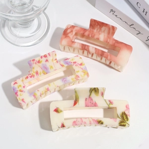 Three elegant large square hair claws with marble and ink floral patterns on a desk