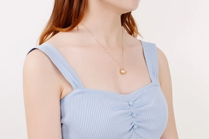 Gros plan sur un collier en titane or rose élégant avec un pendentif perle dorée brillante