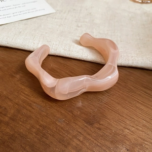 Close-up of pink marble acrylic bangle with irregular wave design on linen fabric