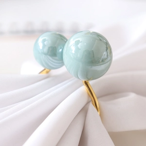 U-shaped turquoise napkin ring with twin faux pearls and gold finish on white fabric