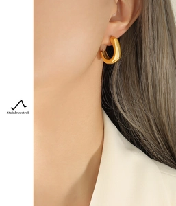 Gros plan d'un mannequin portant des boucles d'oreilles créoles C dorées en acier inoxydable