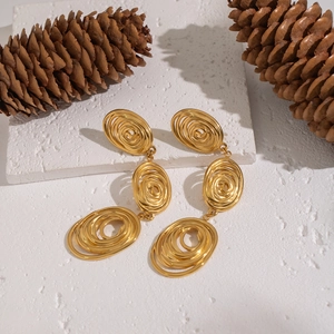 Detailed shot of gold twisted coil earrings on white stone with pine cone background