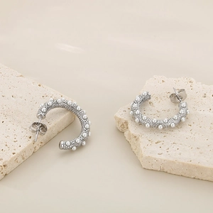 Detail view of silver C-shaped pearl earrings with embossed texture and metal butterfly backs