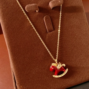 Close-up of a delicate gold chain featuring a red enamel rocking horse pendant on a velvet stand