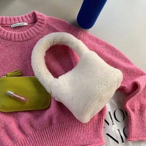 Flat lay of soft white plush handbag with rounded handles on pink knit sweater background
