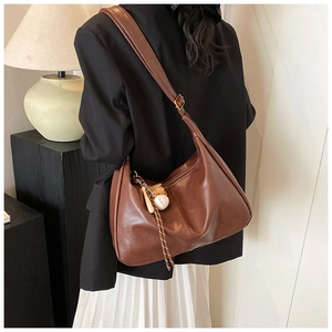 Detail of brown leather crossbody bag with baseball charm and adjustable strap