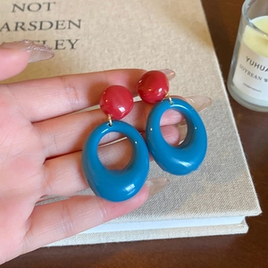 Close-up of red and blue color-block resin drop earrings held against a vintage background