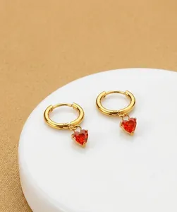 Macro detail of gold hoop earrings with red heart-shaped zircon pendants for women