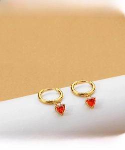 Macro detail of gold hoop earrings with red heart-shaped zircon pendants for women