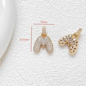 Macro detail of gold letter M pendant with clear zircons and 19x25.5mm measurements