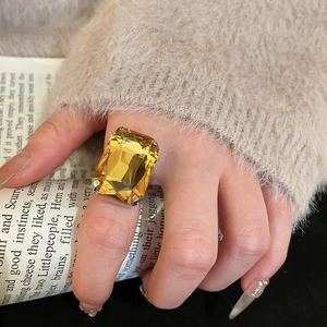 Detailed view of square yellow gemstone ring with silver band held by hand
