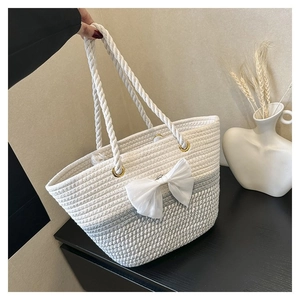 Detail of beige and grey gradient woven tote bag featuring a white bow and thick rope handles