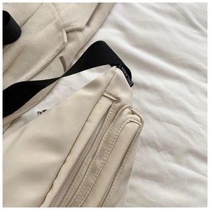 Detailed close-up of beige fabric crossbody bag with black strap and fine stitching