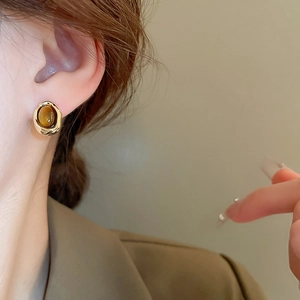 Close-up of retro oval tiger eye stone earrings with gold plating on model's ear