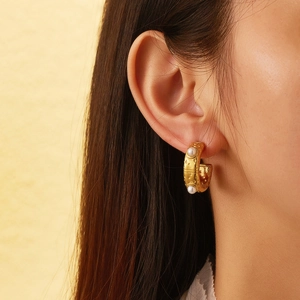 Close-up of golden C-shaped hoop earrings with textured finish and white pearl inlay