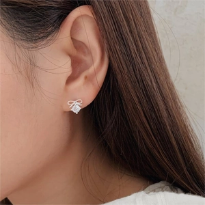 Close-up of elegant silver bow earrings with sparkling round zircon worn on the ear