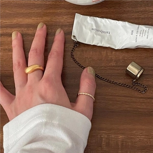 Detail of gold twist rope and wavy rings on fingers with a wooden background