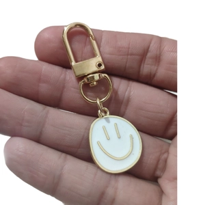 Golden alloy keychain with white oval enamel smiley face pendant held by a hand