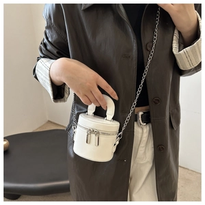Détail d'un sac seau blanc cylindrique avec chaîne argentée et poignée porté par un mannequin