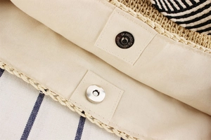 Macro detail of paper rope beach bag showing metal magnetic clasp and beige cotton lining