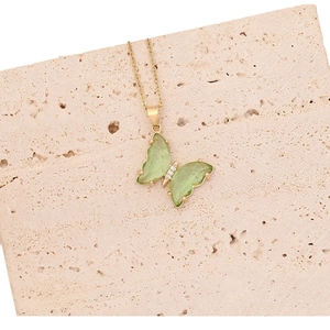 Elegant gold butterfly necklace with green translucent gemstones on a stone surface