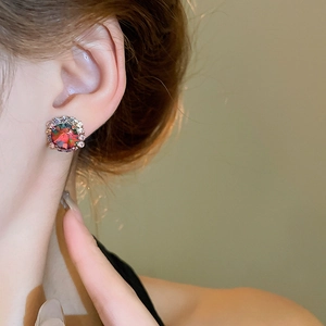Close-up of model wearing round red crystal stud earrings with a halo of small rhinestones
